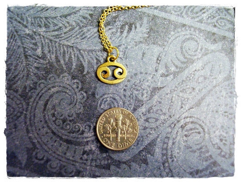 May include: Gold chain necklace with a gold Cancer zodiac sign pendant. The pendant is a stylized crab shape.