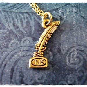 May include: Gold necklace with a charm of a quill pen and ink bottle. The charm says "INK" on the bottle.