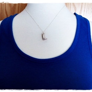 May include: A silver necklace with a boot charm pendant on a mannequin wearing a royal blue tank top.