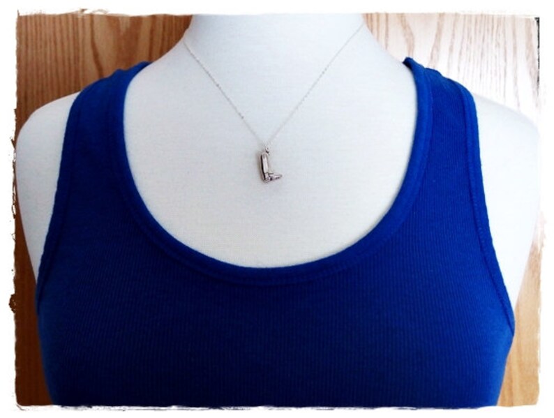 May include: A silver necklace with a boot charm pendant on a mannequin wearing a royal blue tank top.