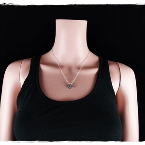 May include: A silver necklace with a small pendant on a mannequin wearing a black vest top against a black background.