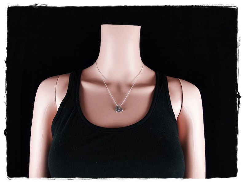May include: A silver necklace with a small pendant on a mannequin wearing a black vest top against a black background.
