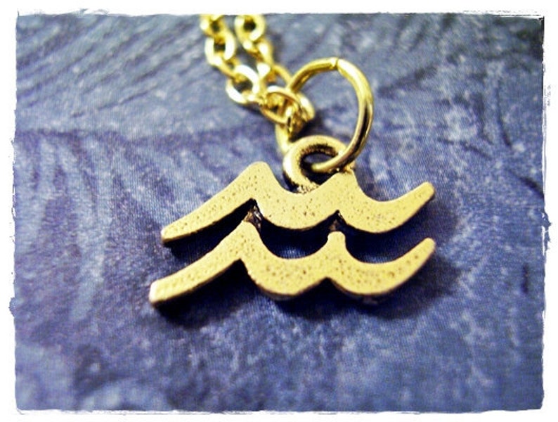 May include: A gold-colored necklace with a pendant shaped like the astrological symbol for Aquarius. The pendant is a double wave design.