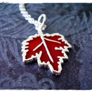 May include: A silver necklace with a red enamel leaf pendant. The leaf is detailed with a white outline and a central vein.