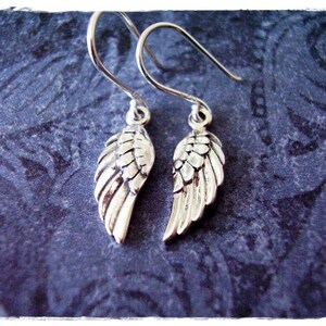 May include: A pair of silver dangle earrings with a detailed wing design. The wings are textured and have a slightly aged look.