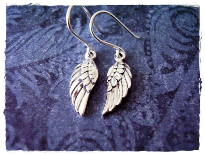 May include: A pair of silver dangle earrings with a detailed wing design. The wings are textured and have a slightly aged look.