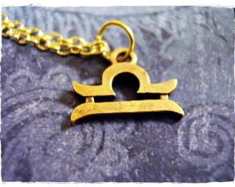 May include: Gold-toned necklace with a Libra zodiac sign pendant. The pendant is a stylized representation of a balance scale.