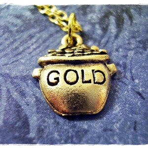Könnte beinhalten: Goldene Topf-Anhänger-Kette mit einer goldenen Kette. Der Topf hat das Wort "GOLD" auf der Vorderseite geprägt.