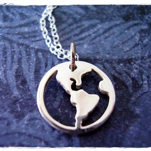 Puede incluir: Un collar de plata con un colgante con forma de la Tierra. El colgante está recortado para mostrar los continentes.