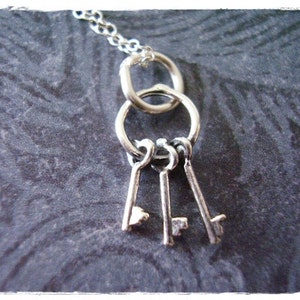 Op de afbeelding: Zilveren ketting met drie sleutels die aan een ketting hangen. De sleutels zijn aan een ring bevestigd.