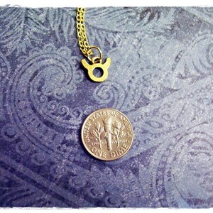 May include: Gold Taurus zodiac sign pendant necklace on a blue patterned background with a US dime for scale.