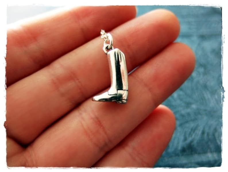 May include: A silver boot charm necklace. The boot charm is detailed and has a pointed toe.