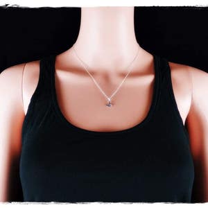 以下が含まれることがあります： 小さなペンダントが付いたシルバーチェーンネックレス。ネックレスは、黒いタンクトップを着た人が着用しています。