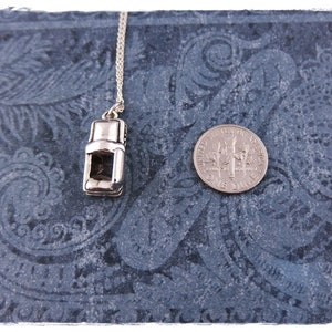 May include: A silver charm necklace featuring a miniature coffee maker pendant. The pendant is detailed with a handle, spout, and a small window. The necklace is displayed on a blue patterned background with a US dime for scale.