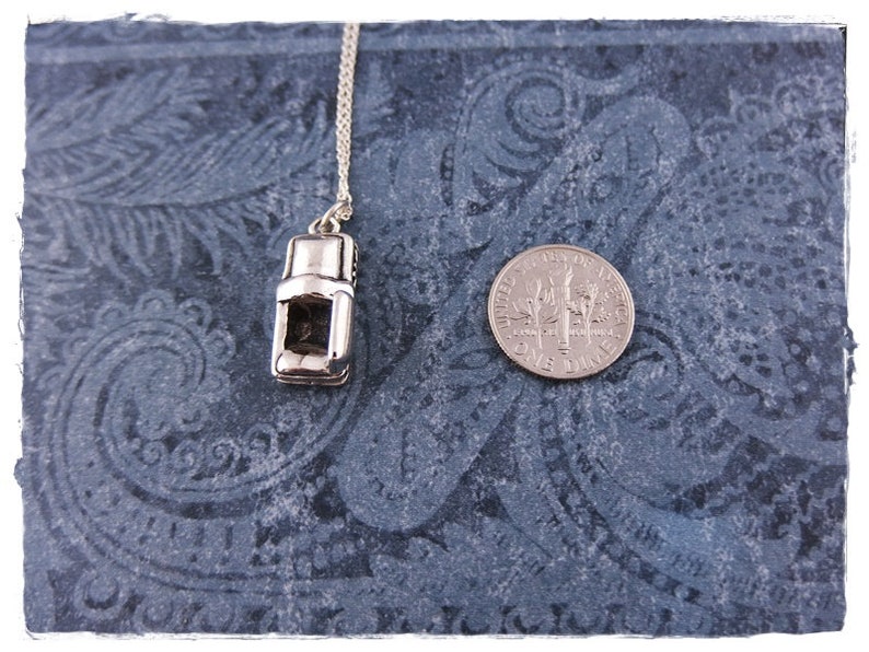 May include: A silver charm necklace featuring a miniature coffee maker pendant. The pendant is detailed with a handle, spout, and a small window. The necklace is displayed on a blue patterned background with a US dime for scale.