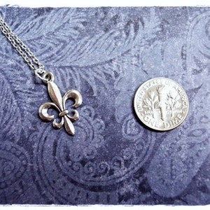 May include: Silver pendant necklace featuring a fleur-de-lis design. The pendant is approximately the size of a ten pence coin.