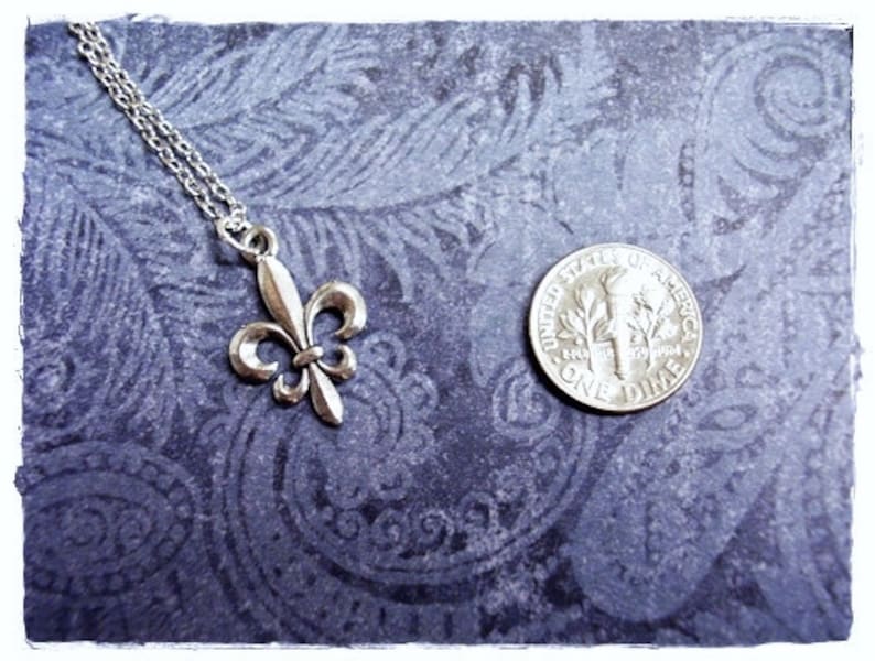 May include: Silver pendant necklace featuring a fleur-de-lis design. The pendant is approximately the size of a ten pence coin.