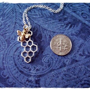 May include: A silver chain necklace with a silver honeycomb pendant and a gold bee charm. The necklace is on a blue patterned background.