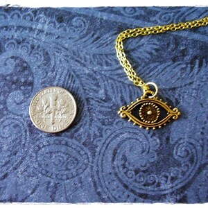 May include: Gold chain necklace with an eye-shaped pendant. The pendant is detailed with a gold circle in the center and a black background.
