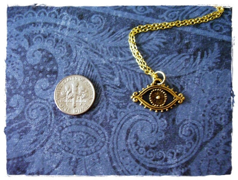 May include: Gold chain necklace with an eye-shaped pendant. The pendant is detailed with a gold circle in the center and a black background.