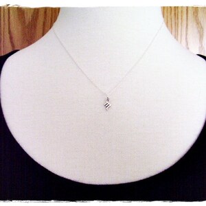 May include: A silver necklace with a small, silver pendant shaped like the letter "M". The necklace is on a white mannequin wearing a black top.
