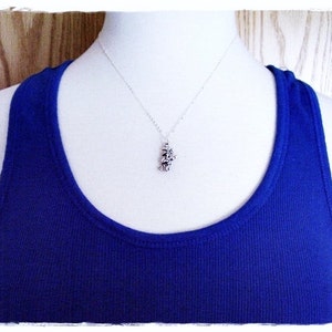 May include: A silver necklace with a small, detailed pendant. The pendant is shaped like a cluster of flowers. The necklace is displayed on a white mannequin wearing a royal blue tank top.