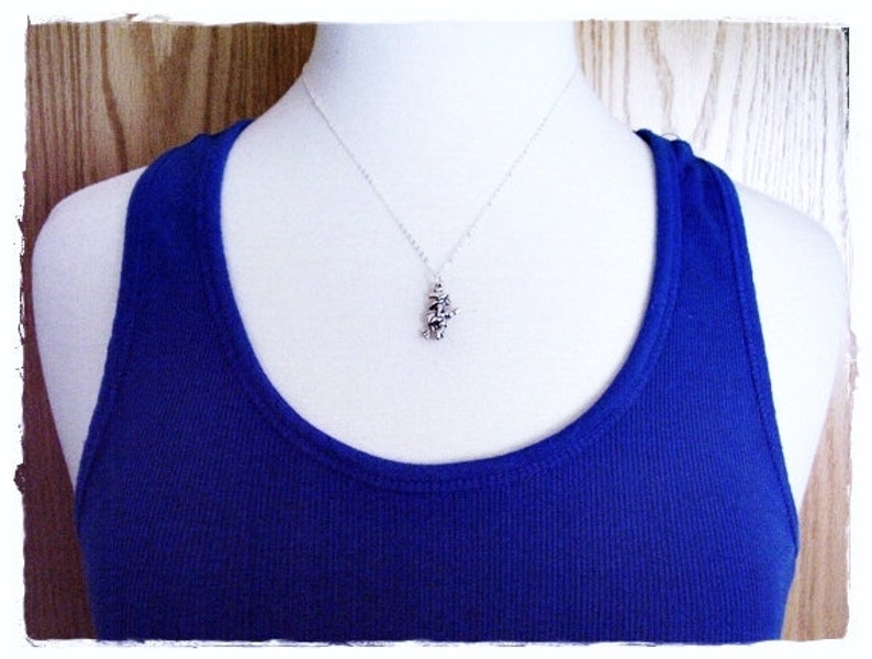 May include: A silver necklace with a small, detailed pendant. The pendant is shaped like a cluster of flowers. The necklace is displayed on a white mannequin wearing a royal blue tank top.