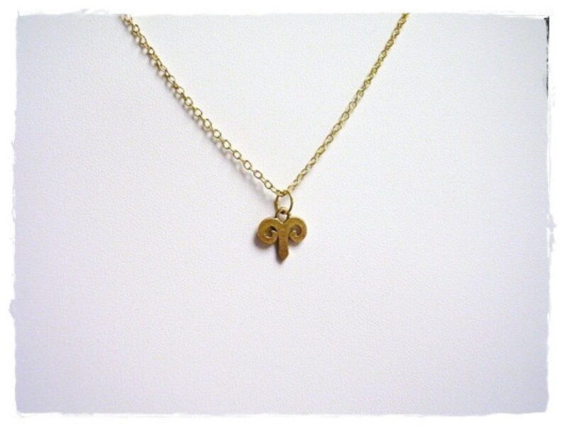 Peut inclure: Un collier en cha&icirc;ne dor&eacute;e avec un petit pendentif en or en forme de cornes de b&eacute;lier.