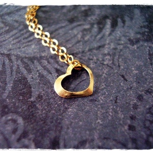 May include: A gold heart pendant necklace with a delicate chain. The necklace is on a dark gray textured background.