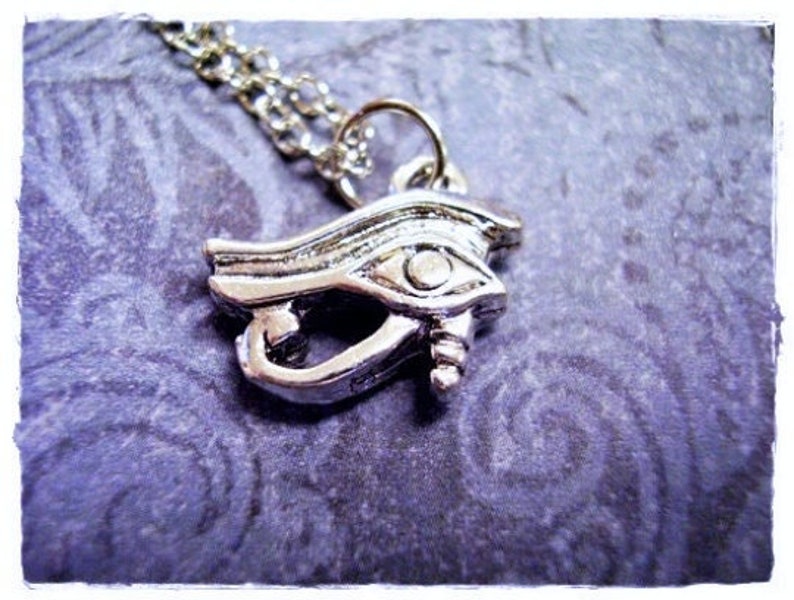 May include: Silver necklace with an eye of Horus pendant. The pendant is detailed with intricate lines and a raised eye.