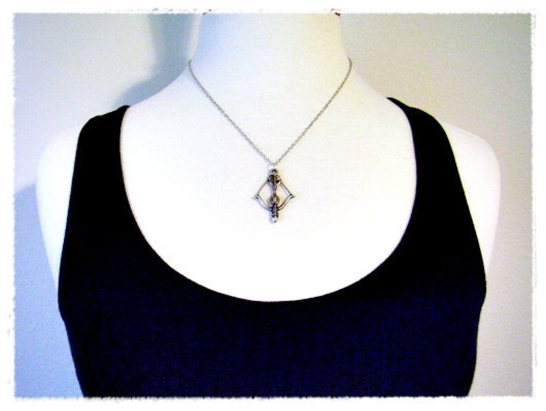 May include: A silver necklace with a geometric pendant featuring a stylized figure. The necklace is worn by a person wearing a black tank top.