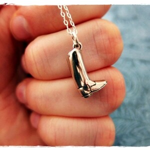May include: A silver charm necklace with a boot pendant. The boot is detailed with a pointed toe and a heel.