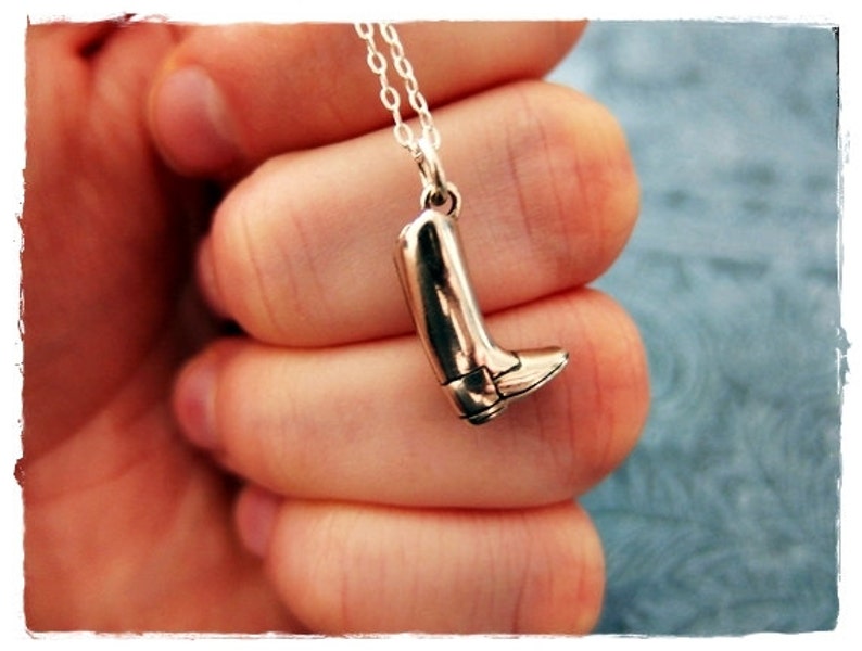 May include: A silver charm necklace with a boot pendant. The boot is detailed with a pointed toe and a heel.