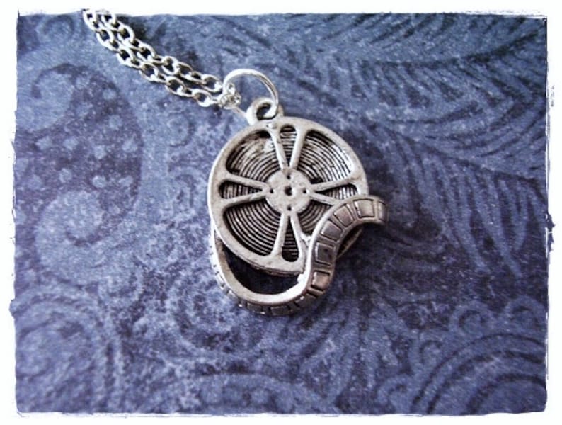 May include: A silver necklace with a film reel pendant. The reel is detailed with a silver film strip.