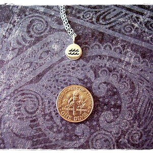 May include: A silver chain necklace with a gold pendant featuring the astrological symbol for Aquarius. The pendant is on a dark patterned background.