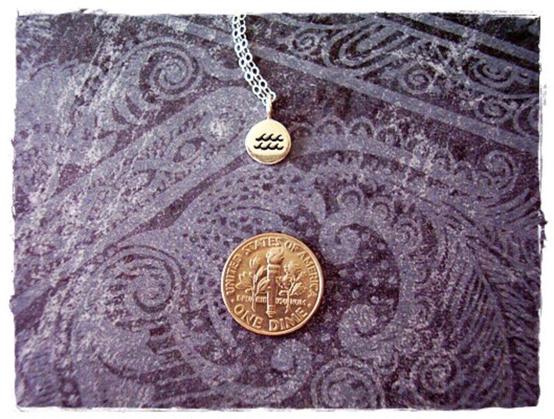 May include: A silver chain necklace with a gold pendant featuring the astrological symbol for Aquarius. The pendant is on a dark patterned background.