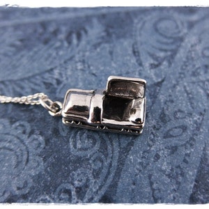May include: A silver charm necklace with a detailed miniature car pendant. The car is open and has a detailed interior.