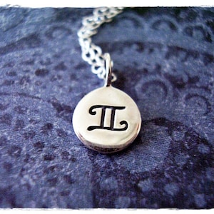 May include: Silver necklace with a round pendant featuring the Gemini zodiac symbol.