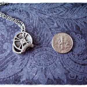 May include: A silver necklace with a film reel pendant. The pendant is about the size of a US dime.