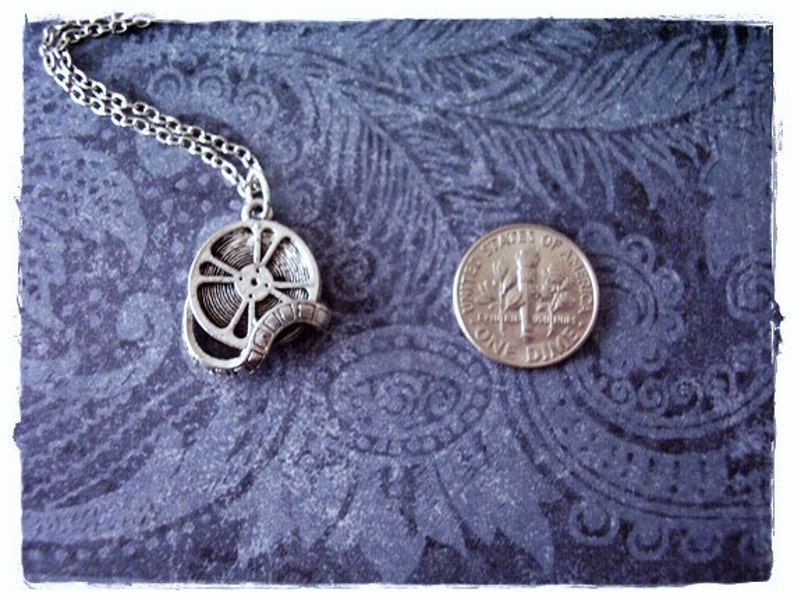 May include: A silver necklace with a film reel pendant. The pendant is about the size of a US dime.