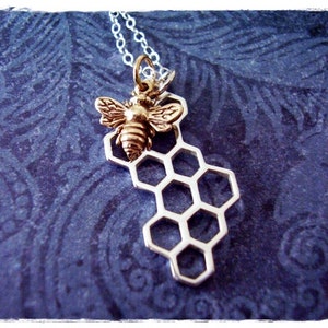 May include: A silver necklace with a gold bee charm on a honeycomb pendant.