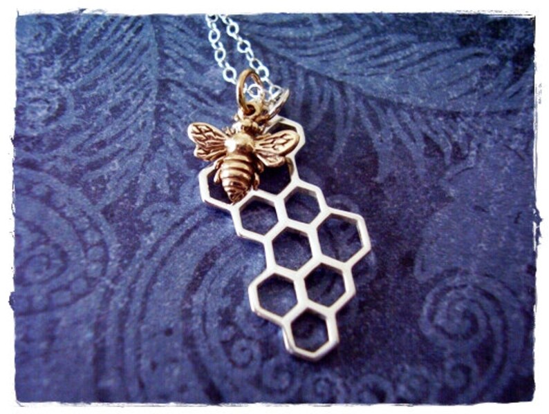 May include: A silver necklace with a gold bee charm on a honeycomb pendant.