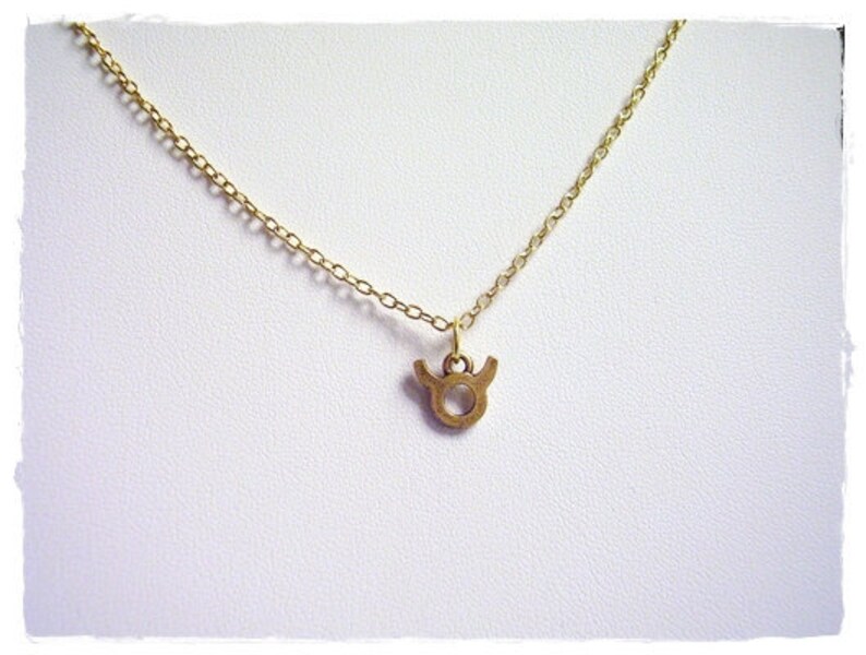 May include: A gold chain necklace with a small gold Taurus zodiac sign pendant.