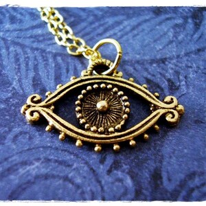 May include: Gold-toned eye pendant necklace with a detailed design. The eye is surrounded by a circle of small beads and has a raised center.
