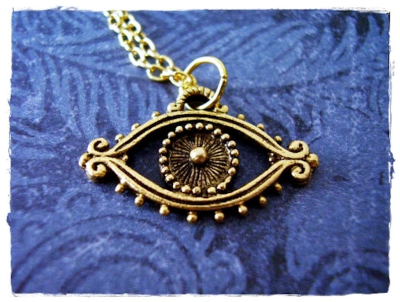 May include: Gold-toned eye pendant necklace with a detailed design. The eye is surrounded by a circle of small beads and has a raised center.
