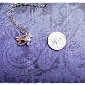 May include: Silver necklace with an eye of Horus pendant on a purple background with a paisley pattern.