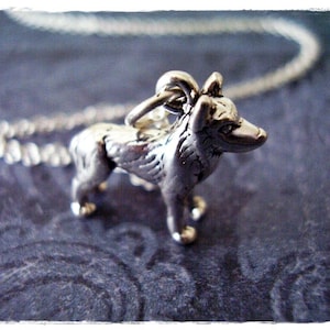 May include: A silver charm necklace featuring a detailed wolf pendant. The wolf is standing on all four paws with its head turned to the side. The chain is silver and has a delicate link design.
