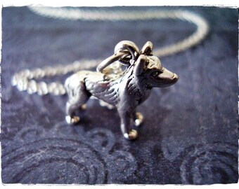 May include: A silver charm necklace featuring a detailed wolf pendant. The wolf is standing on all four paws with its head turned to the side. The chain is silver and has a delicate link design.