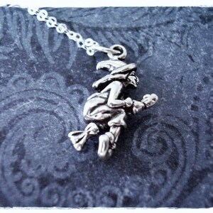 May include: A silver charm necklace featuring a witch riding a broomstick. The charm is detailed and has a vintage look.