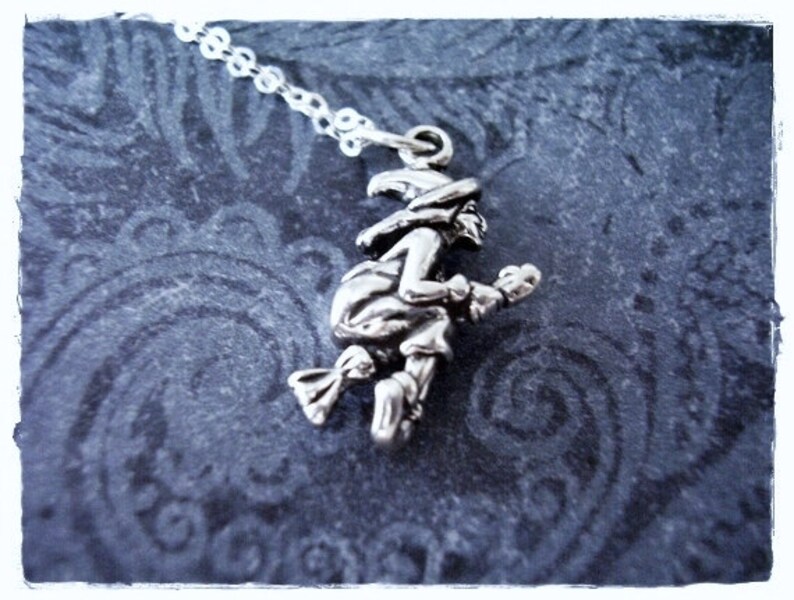 May include: A silver charm necklace featuring a witch riding a broomstick. The charm is detailed and has a vintage look.